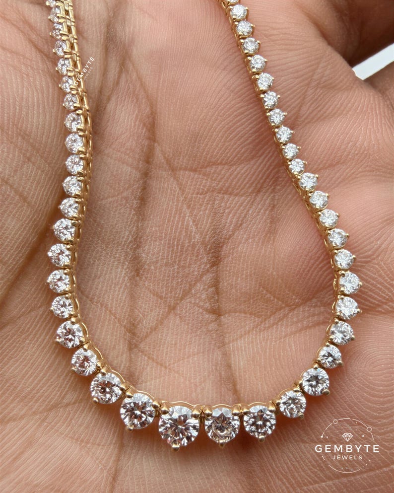 A close-up image of a gold necklace with a row of diamonds on it, held in someone's hand.