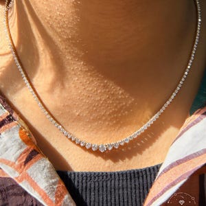 A close-up view of a woman's neck and chest area, featuring a delicate necklace with a row of small diamonds.