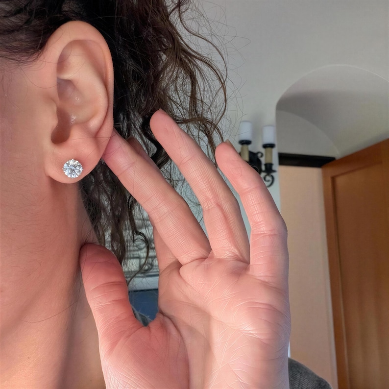 A close-up of a person's hand wearing a diamond earring, with their hair visible behind the ear.