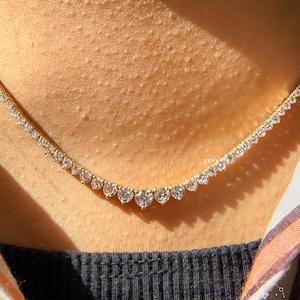 A close-up view of a delicate necklace with numerous small diamonds set in a gold chain, worn around the neck of a person.