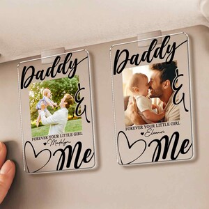 May include: Two clear acrylic car visor photo holders with the words "Daddy & Me" in black script. Each holder features a photo of a father and child, with the text "Forever Your Little Girl" and a name below.
