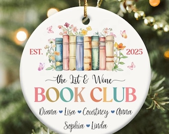 May include: A round white ceramic ornament featuring a row of colorful books topped with watercolor flowers and butterflies. Text reads EST. 2025, the Lit & Wine BOOK CLUB, and lists the names Diana, Lisa, Courtney, Anna, Sophia, and Linda.