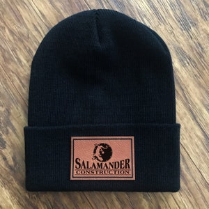 May include: Black knit beanie with a brown leather patch that says "Salamander Construction" with a salamander logo.