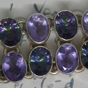 Peut inclure: Un bracelet en argent orn&eacute; de pierres pr&eacute;cieuses ovales dans des tons de violet et de vert iris&eacute;. Les pierres sont serties dans un design de cha&icirc;ne. Le bracelet est un bijou.