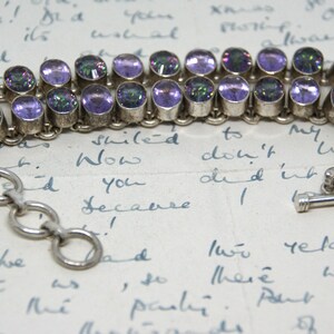 Peut inclure: Bracelet en argent avec deux rang&eacute;es de pierres pr&eacute;cieuses ovales violettes iris&eacute;es. Le bracelet est dot&eacute; d'une cha&icirc;ne et d'un fermoir &agrave; bascule. Le fond est une lettre manuscrite.