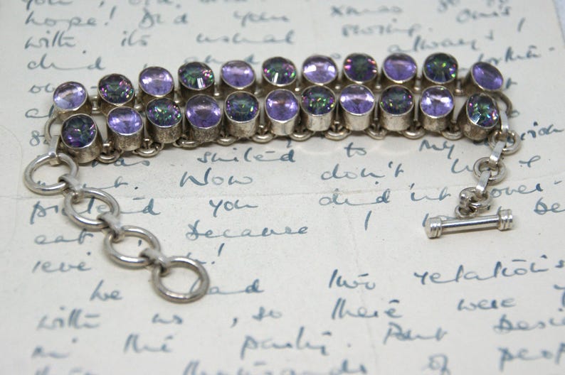 Peut inclure: Bracelet en argent avec deux rang&eacute;es de pierres pr&eacute;cieuses ovales violettes iris&eacute;es. Le bracelet est dot&eacute; d'une cha&icirc;ne et d'un fermoir &agrave; bascule. Le fond est une lettre manuscrite.