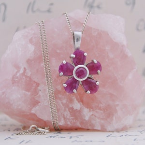 May include: A silver necklace with a pink ruby flower pendant. The pendant has six petals and a round center stone.