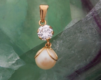 Peut inclure: Un pendentif en or avec une pierre précieuse ronde transparente et une perle blanche suspendue.