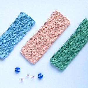 May include: Three knitted headbands in different colors: light blue, peach, and green. Each headband has a unique cable knit pattern.