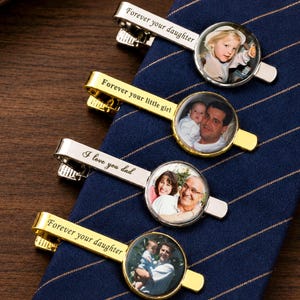 May include: Four metal tie clips with circular photo inserts and engraved text. Two are silver-toned with 'Forever your daughter' and 'I love you dad', and two are gold-toned with 'Forever your little girl' and 'Forever your daughter' text.