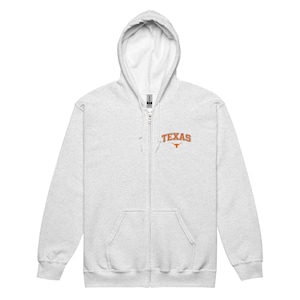 May include: A light gray zip-up hoodie with a white interior hood. The hoodie features the word "TEXAS" in orange block letters with a Longhorn logo. The hoodie has a full zipper and two front pockets.