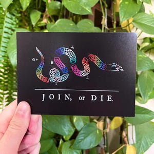 May include: Black rectangular card featuring a segmented rainbow-colored snake illustration. The text "JOIN, or DIE." is printed in white below the snake. The snake's segments are labeled with letters.
