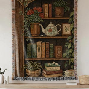 May include: Tapestry throw blanket featuring a detailed illustration of a bookshelf with books, plants, and a teapot. The color palette includes browns, greens, and reds, creating a cozy, vintage aesthetic. The edges are fringed.