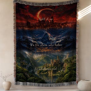 May include: A woven throw blanket featuring a three-tiered landscape illustration. The top section shows a city under a red moon with the text light it up. The middle shows mountains and stars with the text To the stars who listen. The bottom shows a castle by a lake with the text to whatever end.