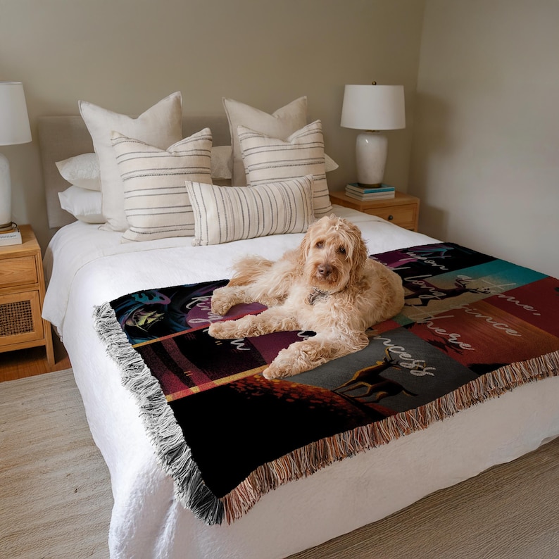 Puede incluir: Una manta tejida con un dise&ntilde;o de patchwork con texto e ilustraciones en tonos negros, rojos y turquesas. La manta tiene un borde con flecos y est&aacute; sobre una cama. Un perro est&aacute; acostado sobre la manta.