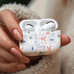 May include: White AirPods Pro case with a colorful pattern of sea creatures and stamps, with the name "Stacy" in cursive. The case is open, revealing the white earbuds inside.