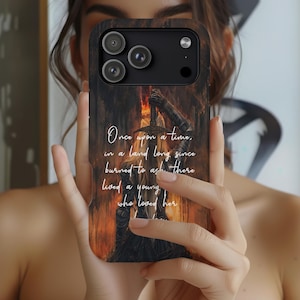 May include: A phone case with a dark wood grain design. The case features a fantasy-themed illustration of a figure holding a sword with flames, and the text "Once upon a time, in a land long since burned to ash there lived a young who loved her."