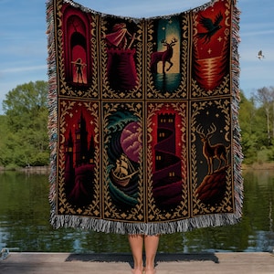 May include: A woven throw blanket featuring eight distinct rectangular panels with fantasy-themed illustrations including castles, a ship on waves, a deer, and a bird, all framed by gold floral borders with a fringed edge on the top and bottom.
