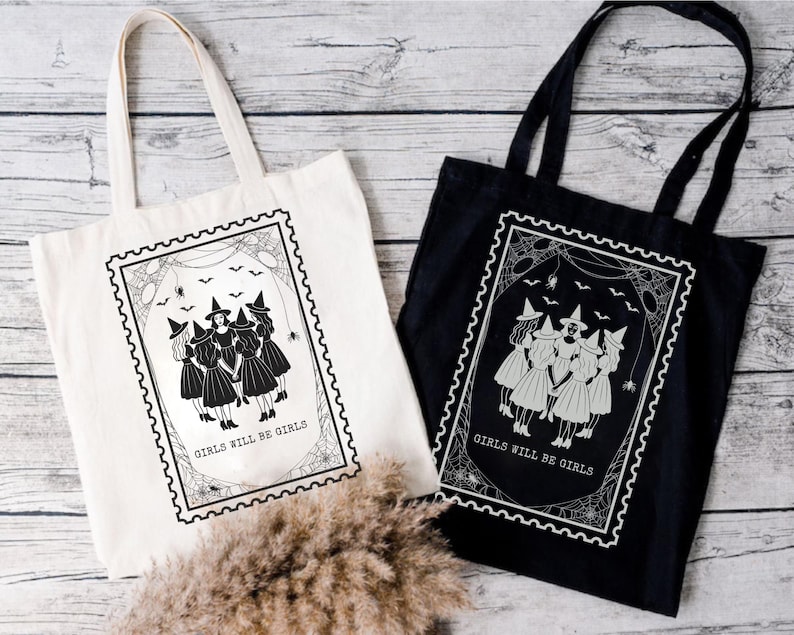 May include: Two tote bags, one cream and one black, with a witch-themed design. Each bag features a framed illustration of five witches in dresses and hats, with the text "GIRLS WILL BE GIRLS". The design includes spiderwebs and bats.