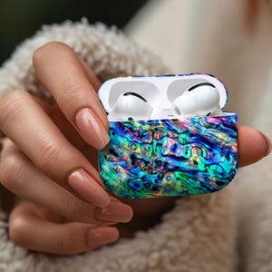 May include: A colorful, iridescent case for wireless earbuds. The case is open, revealing white earbuds inside. The case features a swirling pattern of blues, greens, and purples, creating a vibrant, eye-catching design.