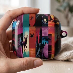 May include: A colorful AirPod case featuring a collage of fantasy-themed illustrations. The design includes images of a deer, a castle, and other scenic elements in shades of red, orange, purple, and blue. The case is held in a hand.