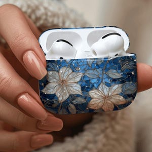 May include: AirPods Pro case with a blue floral design. The case features a mosaic-style pattern with white and gold-colored flowers and leaves. The AirPods are white and visible inside the open case.