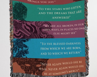 May include: A woven throw blanket featuring five horizontal color-blocked sections in red, teal, purple, blue, and brown. Each section displays a literary quote and a graphic illustration, including a wolf, a dagger, and a mask, with fringed edges.