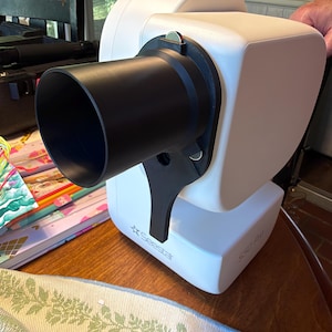 May include: A white Seestar S50 Pro smart telescope featuring a black cylindrical lens hood attached to the front. The device has a rounded, compact body with the brand name Seestar printed on the base and the model name S50 Pro on the side.