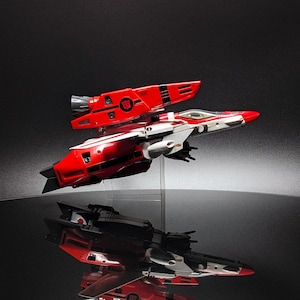 Peut inclure: Un avion de chasse jouet rouge, blanc et noir avec un design détaillé. L'avion a une forme aérodynamique élégante avec une section supérieure proéminente. Le jouet est présenté sur un fond sombre, avec son reflet visible en dessous.