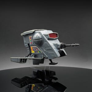 Könnte beinhalten: Ein graues und schwarzes Star Wars Imperial Speeder Bike Spielzeug mit einem roten Licht vorne und einer schwarzen Waffe an der Seite. Das Spielzeug steht auf einem durchsichtigen Plastikständer.