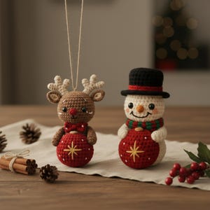 Puede incluir: Dos adornos navideños de ganchillo: un reno y un muñeco de nieve. El reno es marrón con una pajarita roja y una bola roja con una estrella dorada. El muñeco de nieve tiene un sombrero negro, una bufanda verde y roja y una bola roja con una estrella dorada.