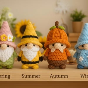 May include: Four crochet gnomes representing the seasons: Spring, Summer, Autumn, and Winter. Each gnome has a unique hat and outfit in corresponding colors. The gnomes are displayed on a wooden shelf with the season names below.
