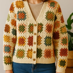 May include: Cream crochet cardigan with a V-neck and wooden buttons. The cardigan has colourful square patterns in orange, green, yellow, and brown. A cosy, handmade garment for autumn or winter.