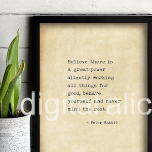 May include: A framed print with the quote "Believe there is a great power silently working all things for good, behave yourself and never mind the rest." The print is in a black frame and sits on a wooden surface. A potted plant is to the left.