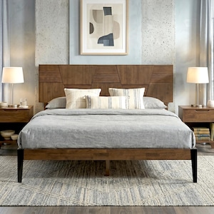 May include: A wooden bed frame with a headboard featuring horizontal slats and geometric panels. The bed is dressed in a light gray comforter with two cream-colored pillows with thin stripes and a central rectangular pillow with matching stripes.