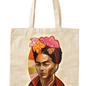 May include: Beige tote bag featuring a portrait of Frida Kahlo with a floral headdress. The portrait is set against an orange and yellow background, with the name "Frida Kahlo" in a cursive font below the image. The bag has two beige handles.