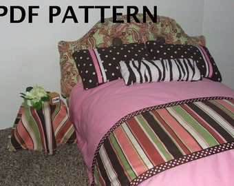 May include: A pink doll bed with a paisley headboard and a striped footboard. The bed has a pink blanket with a brown, green, and pink striped border. There are three pillows on the bed: one with brown polka dots, one with a zebra print, and one with a paisley print. A small side table with a striped cover sits next to the bed.