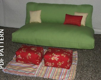 May include: A green fabric sofa with two pillows, one cream and one red, and two red floral patterned cushions. The sofa is sitting on a brown carpet.