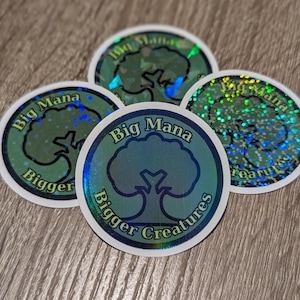 May include: Four round stickers with a holographic effect. Each sticker features a tree graphic within a blue circle, with the words "Big Mana" and "Bigger Creatures" in a white font. The stickers have a shiny, iridescent finish.