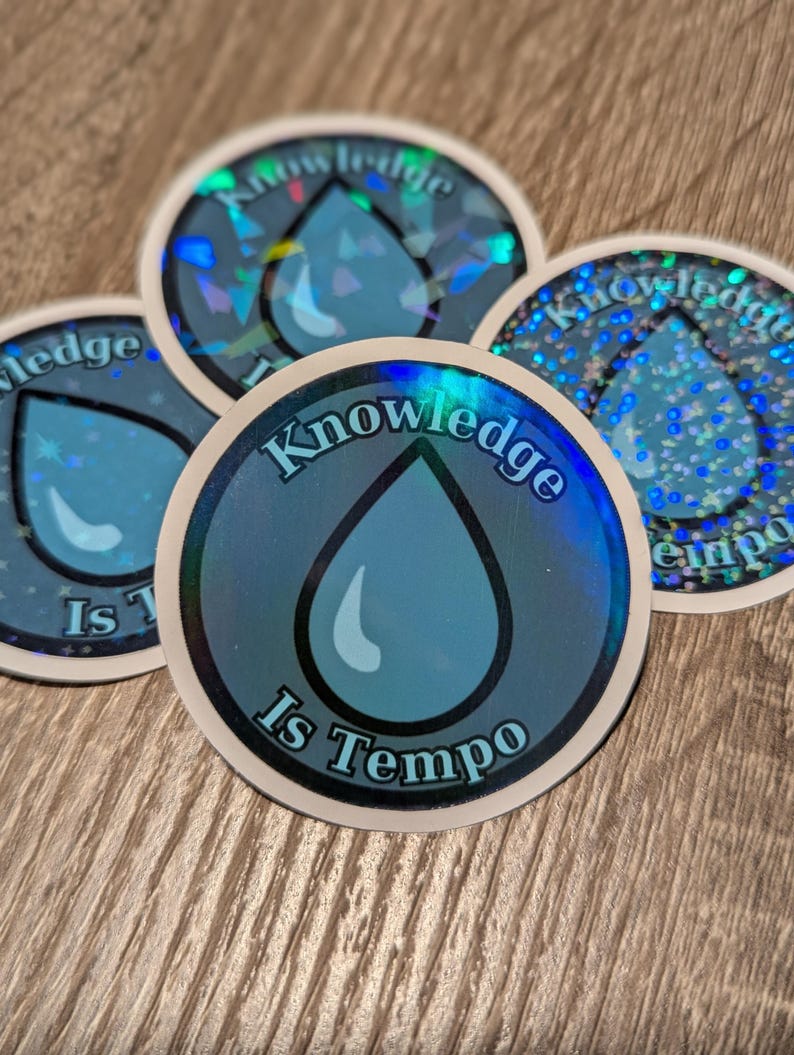 May include: Four round stickers with a blue water drop design and the text "Knowledge Is Tempo". The stickers have a holographic, iridescent finish, with a white border. The stickers are on a wooden surface.