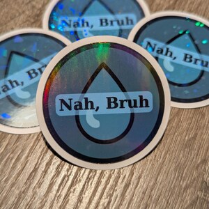 May include: A collection of round stickers with a holographic border and a blue water droplet design. The text "Nah, Bruh" is printed in a white, sans-serif font on a blue background. The stickers are arranged on a wooden surface.