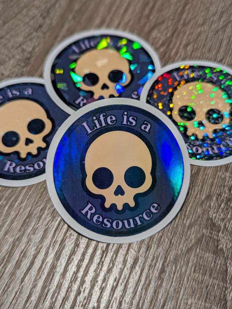 May include: A collection of circular stickers with a skull design. The stickers have a holographic effect with a blue and gold color scheme. The text "Life is a Resource" is printed on the stickers.