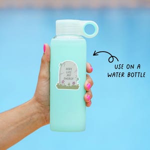 May include: A light blue water bottle with a white lid and handle is held against a blue background. A sticker on the bottle reads "Here Lies My Energy" with a tombstone design. The text "USE ON A WATER BOTTLE" is also visible.