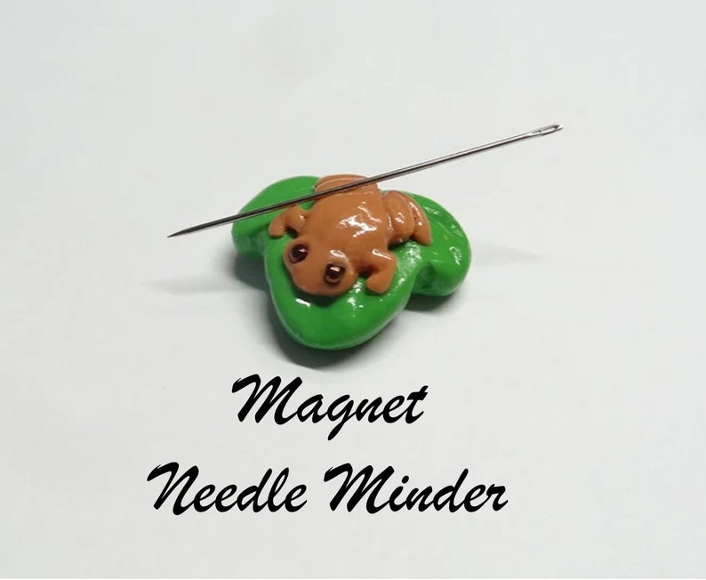 May include: A green frog sitting on a green leaf with a needle stuck in it. The frog and leaf are magnetic and are used as a needle minder for sewing.
