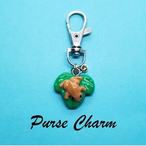 May include: A green leaf charm with a brown frog on it. The charm is attached to a silver key chain with a silver clasp. The charm is a purse charm.