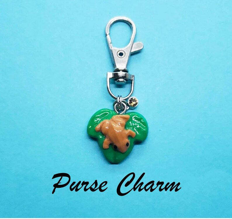 May include: A green leaf charm with a brown frog on it. The charm is attached to a silver key chain with a silver clasp. The charm is a purse charm.