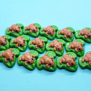 May include: A collection of 15 brown frog figurines on green lily pad bases. The frogs are all in a similar pose, with their legs outstretched and their heads tilted up.