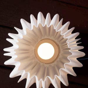 May include: A white, flower-shaped ceiling light fixture with a central light source. The fixture has a ruffled, petal-like design and is mounted against a dark brown wooden surface.