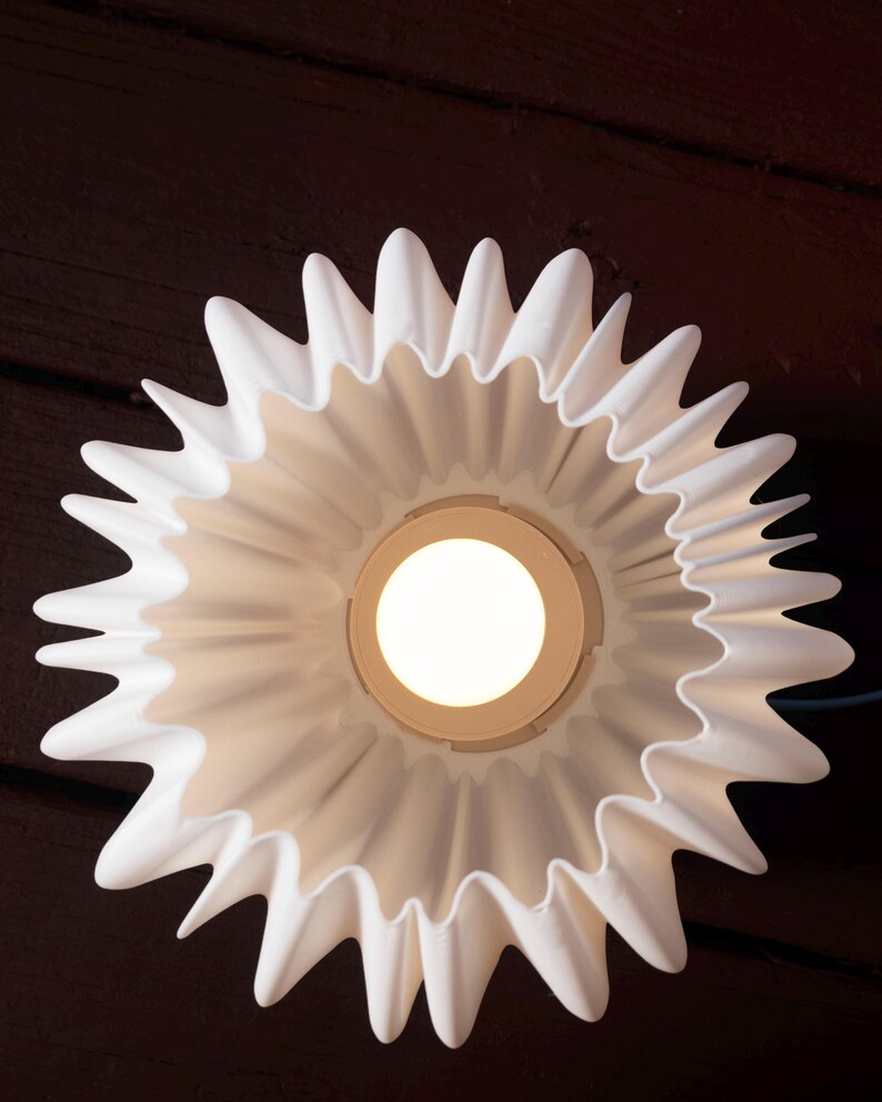 May include: A white, flower-shaped ceiling light fixture with a central light source. The fixture has a ruffled, petal-like design and is mounted against a dark brown wooden surface.