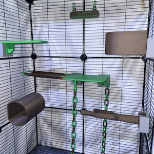 May include: A black wire pet cage interior featuring green and brown plastic accessories, including platforms, a tunnel, a hanging bridge, and two chains. A small sign at the top reads WELCOME TO GLIDERAMAZING.COM in green and brown text.